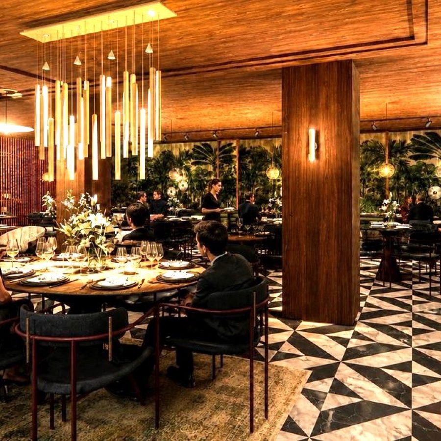 The main dining room at Bey Steakhouse, Paris: round tables under a cluster of brass pendants, with a chequered marble floor and green velvet walls