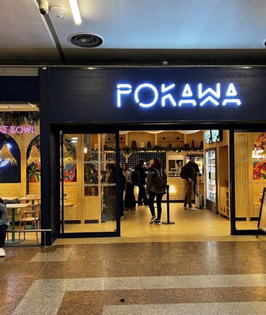 The Pokawa storefront on the concourse at Lyon Part-Dieu station, its neon sign above a timber-lined dining area
